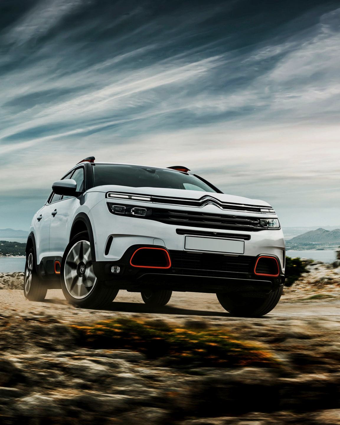 En vit Citroën C5 Aircross på en klippväg vid havet under en dramatisk himmel.